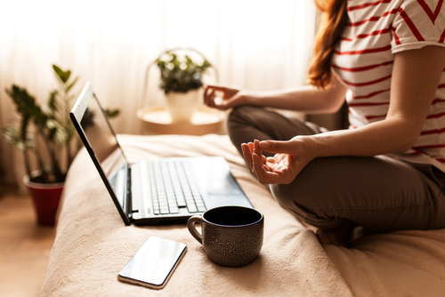 Frau sitzt in Meditationsposition vor Laptop während einer Meditation im Coaching im Online-Coaching.
