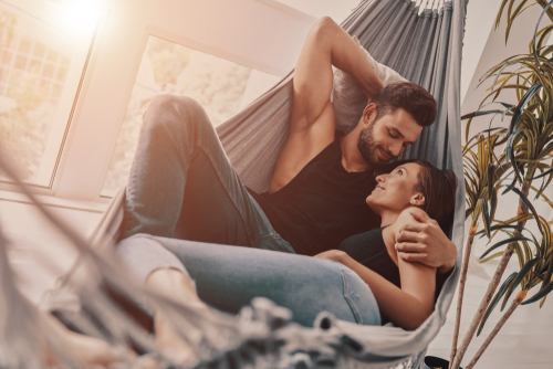 Ein junges Paar liegt in einer Hängematte. Der Mann hält die Frau im Arm, beide lächeln sich an.