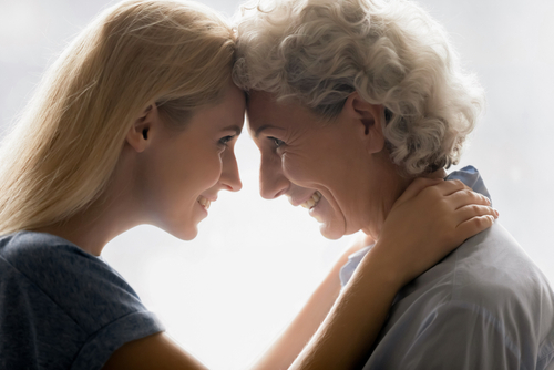 Nahaufnahme im Seitenprofil: Eine erwachsene Tochter und ihre Mutter stehen sich liebevoll gegenüber und halten ihre Stirn zusammen