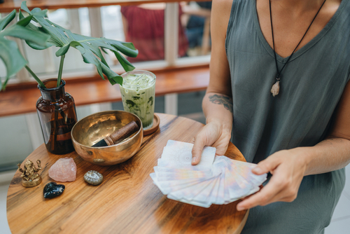 Spirituelle Beratung: Frau hält Tarotkarten in den Händen, auf dem Tisch steht eine Klangschale und Steinen