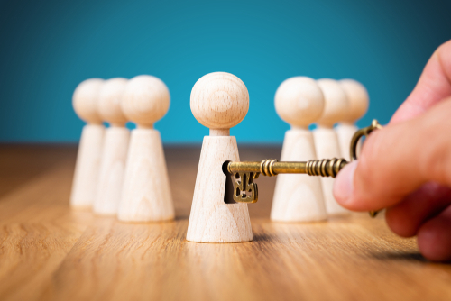 Hand hält einen Schlüssel und öffnet das Schloss einer Holzfigur, symbolisiert systemische Beratung, Coaching und das Freisetzen von Potenzial